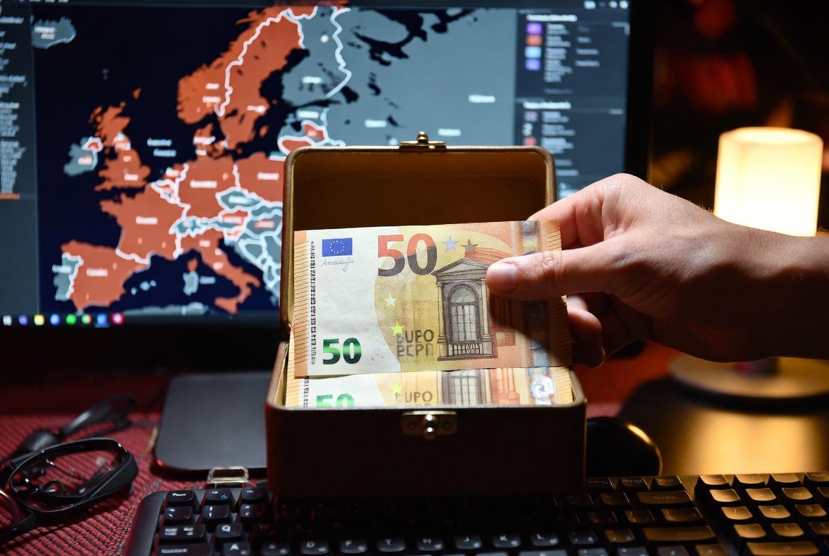 🎨 Portada Sugerida (16:9) Descripción: Un plano detalle de una mano guardando dos billetes de 50 euros dentro de una caja metálica pequeña o un cajón de madera. Al fondo, la pantalla de una computadora muestra un mapa de Europa con zonas de calor. Estética de sobriedad y realismo, con luz de hogar nocturna. Sin texto.
