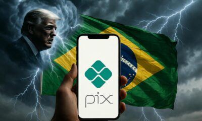 Una ilustración geopolítica dramática en 16:9. En el centro, un smartphone moderno sostenido por una mano firme; la pantalla del teléfono brilla intensamente con el logo de Pix en verde diamante. Detrás del teléfono, la bandera de Brasil se despliega majestuosamente como un escudo protector hecho de luz tejida. Desde la izquierda, nubes de tormenta oscuras con la silueta de Donald Trump lanzan rayos plateados que rebotan contra el escudo de la bandera. Estética de ciber-seguridad, colores vibrantes (verde, amarillo, azul) contrastando con grises metálicos. Sin text