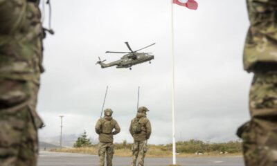 Soldados observan un helicóptero junto a la bandera de Groenlandia
