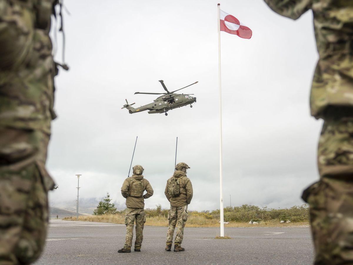 Soldados observan un helicóptero junto a la bandera de Groenlandia