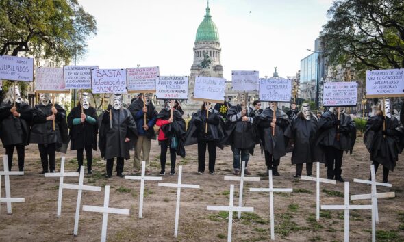 Manifestantes con túnicas negras y máscaras junto a cruces blancas frente al Congreso Nacional