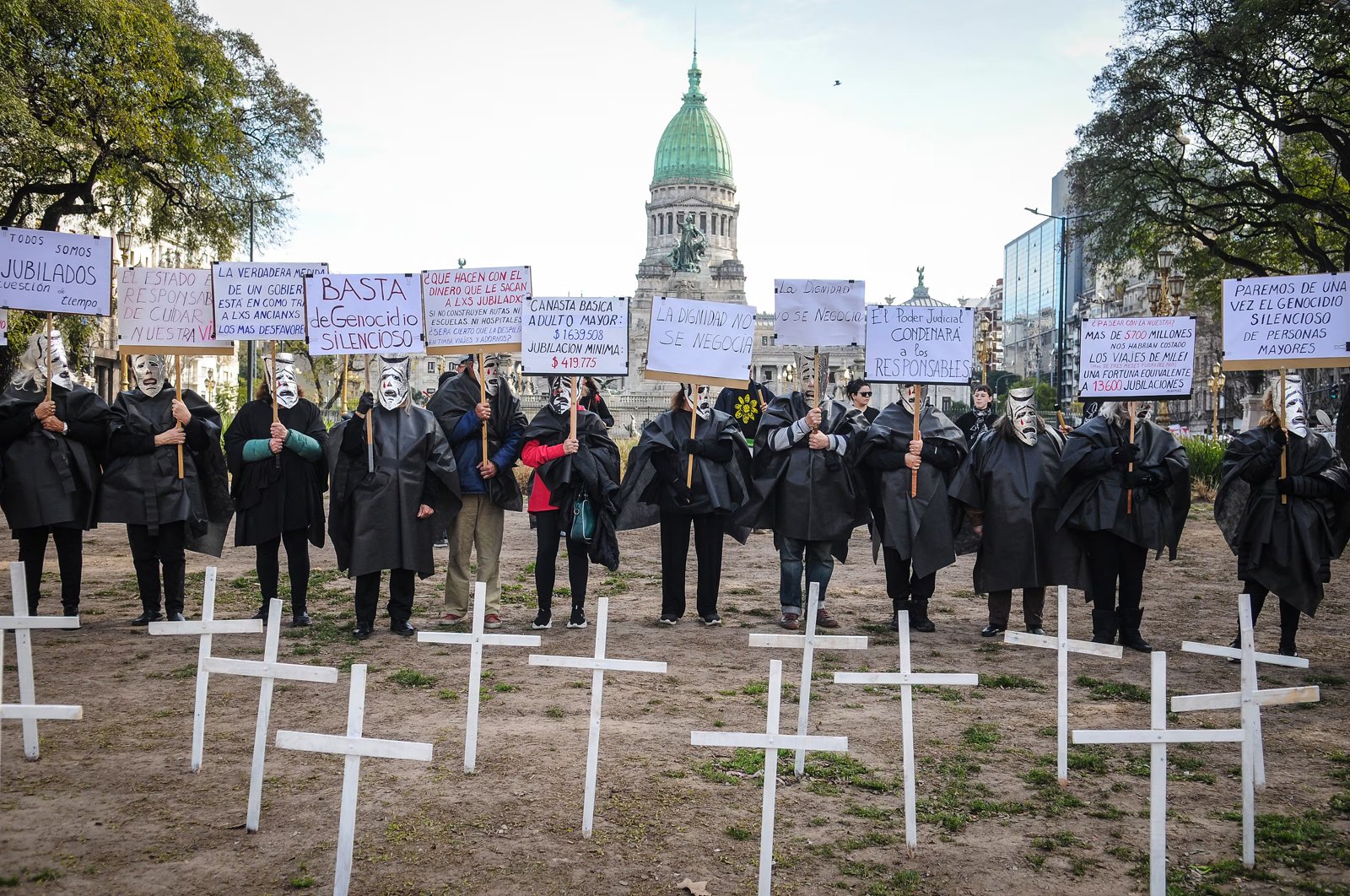 Manifestantes con túnicas negras y máscaras junto a cruces blancas frente al Congreso Nacional