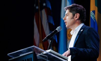 Axel Kicillof habla en un atril con banderas de Argentina, Estados Unidos y Brasil, sobre su viaje a Nueva York