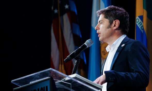Axel Kicillof habla en un atril con banderas de Argentina, Estados Unidos y Brasil, sobre su viaje a Nueva York