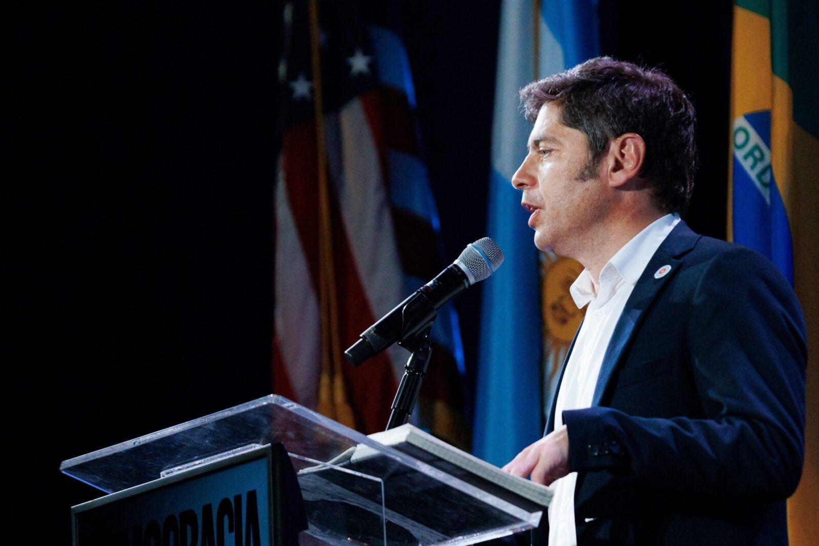 Axel Kicillof habla en un atril con banderas de Argentina, Estados Unidos y Brasil, sobre su viaje a Nueva York