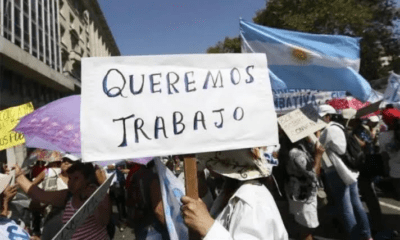 Manifestante sostiene un cartel que dice Queremos Trabajo junto a una bandera argentina