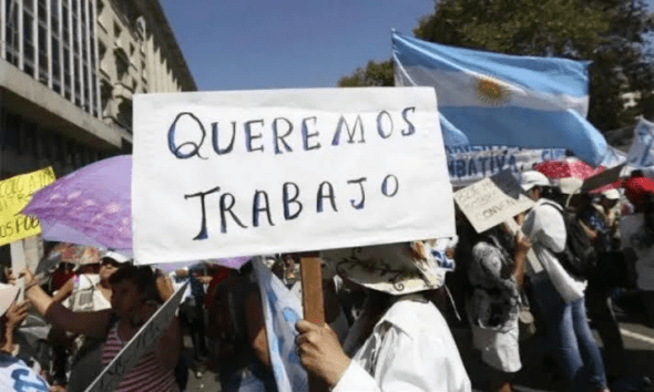 Manifestante sostiene un cartel que dice Queremos Trabajo junto a una bandera argentina