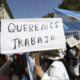 Manifestante sostiene un cartel que dice Queremos Trabajo junto a una bandera argentina